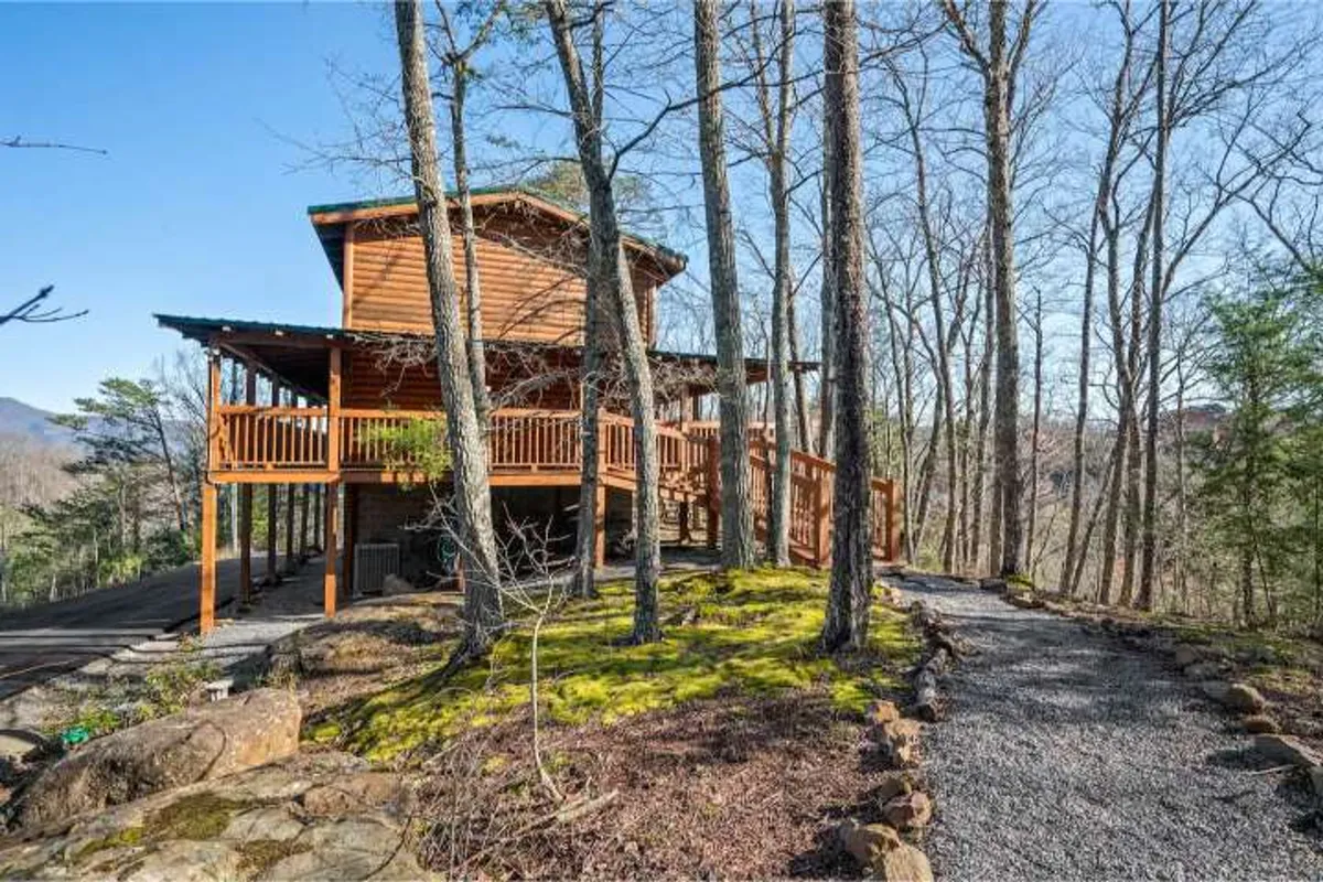A welcoming exterior shot of a wooden cabin nestled among tall trees, with a gravel pathway leading up to a spacious deck area. The setting feels tranquil and private, surrounded by natural beauty, offering a glimpse of the kind of peaceful seclusion described in the section.