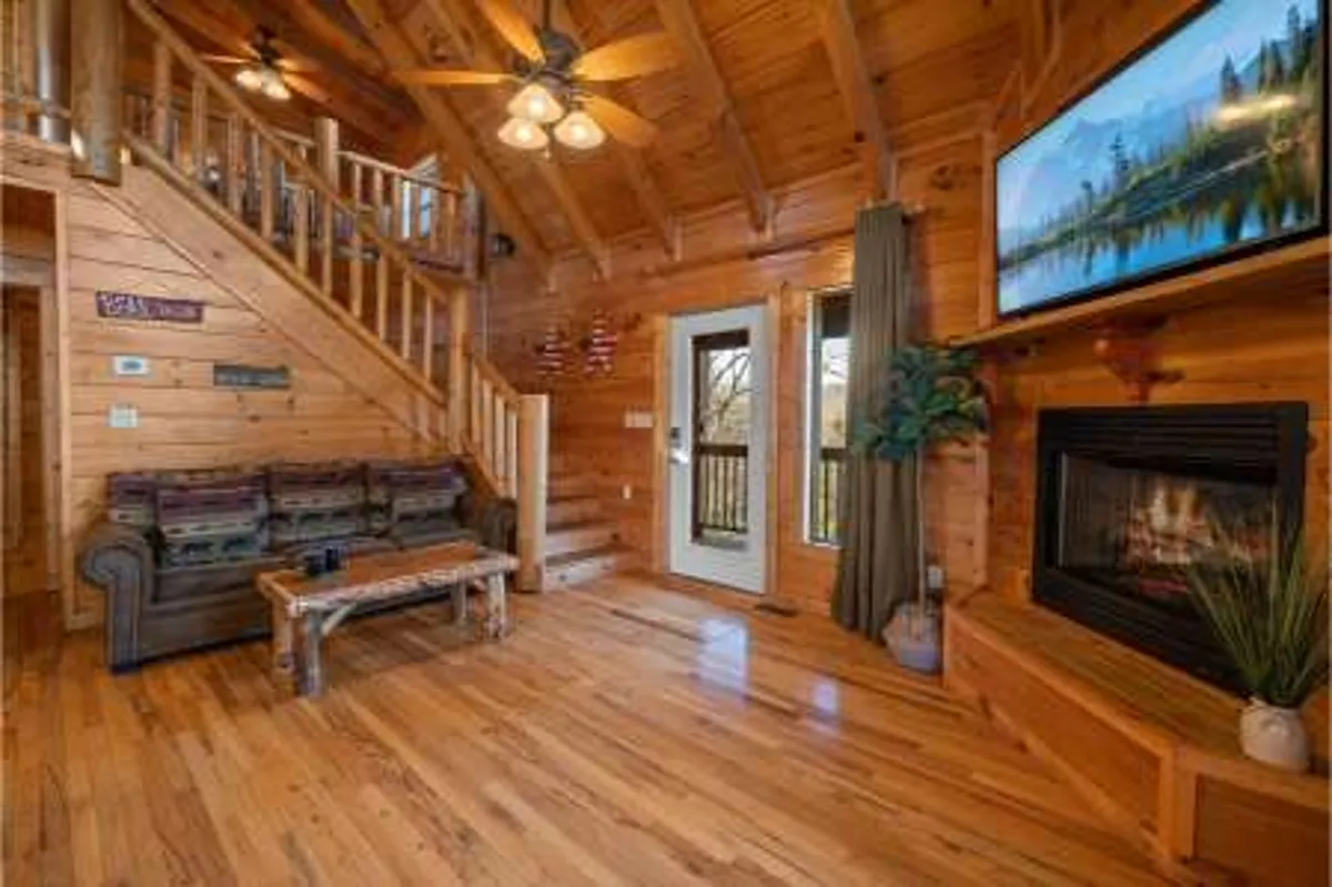 A cozy media area featuring a wooden staircase, a fireplace, a plush sofa, a TV, and large windows letting in natural light. The space is arranged for family gatherings, movie nights, and relaxation, with a warm and inviting atmosphere.