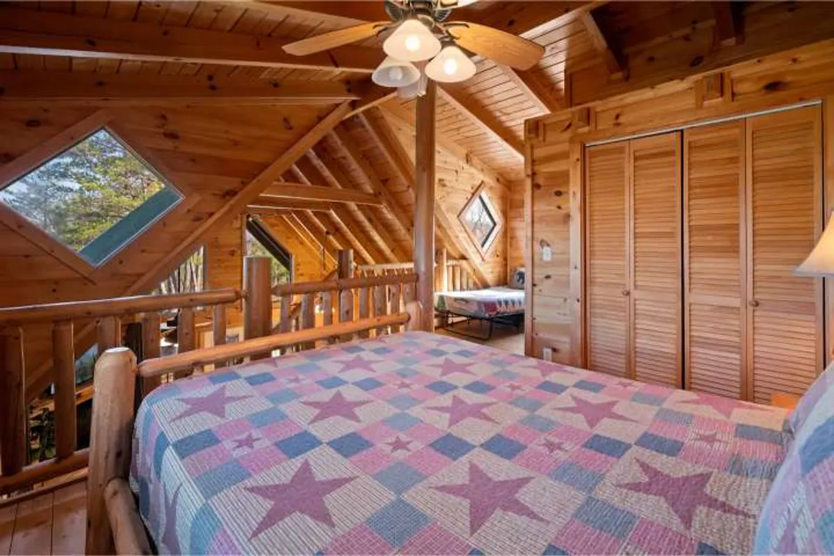 A charming mountain-inspired bedroom with a wooden bed frame, a star-patterned quilt, unique diamond-shaped windows, and exposed wooden beams. The room exudes warmth and invites relaxation, with morning light filtering in for a serene effect.