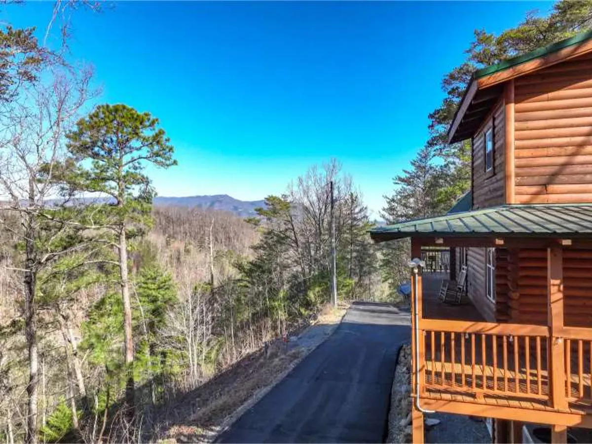 A tranquil exterior shot showcasing a classic log cabin nestled among trees with a sweeping mountain landscape in the background. The setting suggests access to nature trails and ample outdoor space for pets to play and owners to relax while admiring the mountain views.