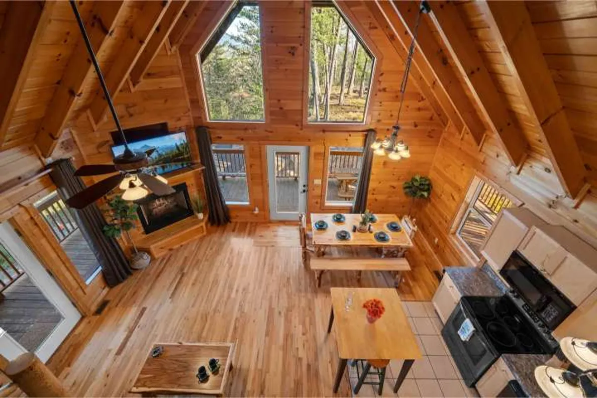 An open-concept dining and kitchen area featuring a rustic wooden table, high-backed chairs, and a modern kitchen with ample counter space. Large windows bring in natural light and offer views of the surrounding landscape. The fireplace adds coziness, and the seamless flow between dining, kitchen, and living areas encourages communal activities.
